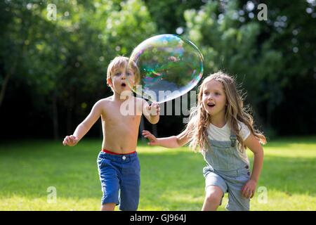 PROPERTY RELEASED. MODEL RELEASED. Brother and sister chasing bubbles in garden. Stock Photo