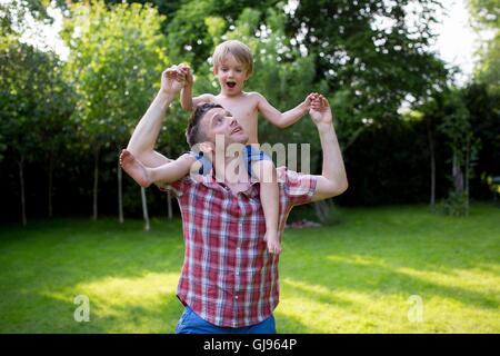 PROPERTY RELEASED. MODEL RELEASED. Father carrying son on his shoulders in the garden. Stock Photo