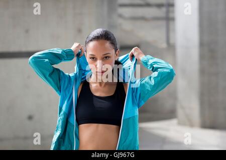 MODEL RELEASED. Young woman putting on hooded top after exercise. Stock Photo