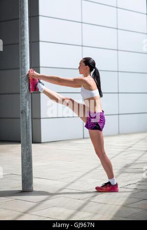 MODEL RELEASED. Young woman stretching leg against post. Stock Photo