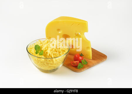 bowl of grated cheese and cheese wedge on wooden cutting board Stock Photo