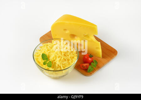 bowl of grated cheese and cheese wedge on wooden cutting board Stock Photo