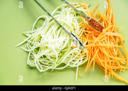Spiralized courgette zucchini and carrot on green chopping board background with stainless steel serving tongs on top Stock Photo