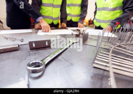 Business man and workers on factory look at documents at table with working tools Stock Photo