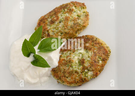 Broccoli and cheese pancakes served with traditional Greek yogurt on a white plate closeup. Stock Photo