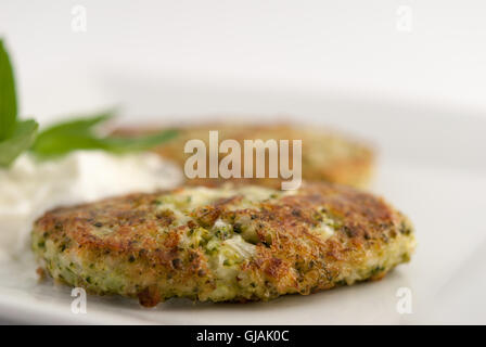 Broccoli and cheese pancakes served with traditional Greek yogurt on a white plate closeup. Stock Photo