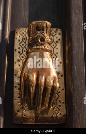 Golden brass hand-shaped door knocker on black wooden door closeup. Kato Drys. Cyprus. Stock Photo