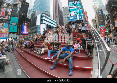 People are sitting on the red steps over a ticket booth on Times Square. Stock Photo