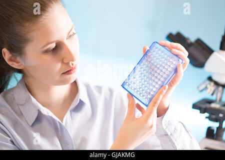 Scientist holding an open 96 well plate with samples, laboratory assistant examining a PCR microplate in hand Stock Photo