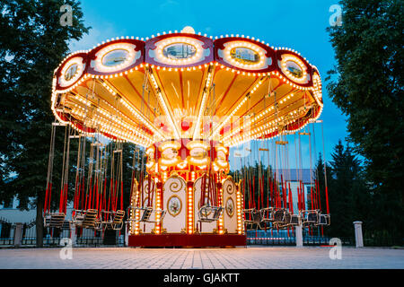 The Brightly Illuminated  Empty Carousel Merry-Go-Round With Seats Suspended On Chains Without People Waiting For Its Visitors. Stock Photo
