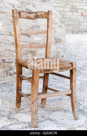 Old shabby wooden straw chair with cobblestone as a background closeup. Stock Photo