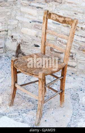 Old shabby wooden straw chair with cobblestone as a background closeup. Stock Photo