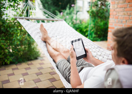 Man using e-book with lorem ipsum text on screen while relaxing in a hammock. Stock Photo
