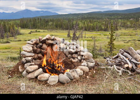 Campfire in a rock ring overlooking a valley view in the Yukon Territory of Canada in summer. Stock Photo