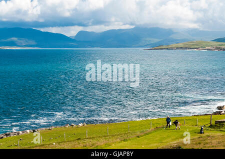 Two golfers teeing off at Isle Of Harris Golf Course in the Outer Hebrides with Sound of Taransay and North Harris in background Stock Photo