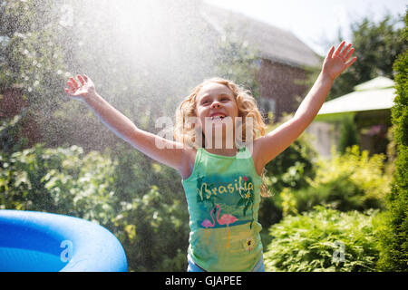Preschooler cute girl playing with garden sprinkler. Summer outdoor water fun in the backyard. Stock Photo