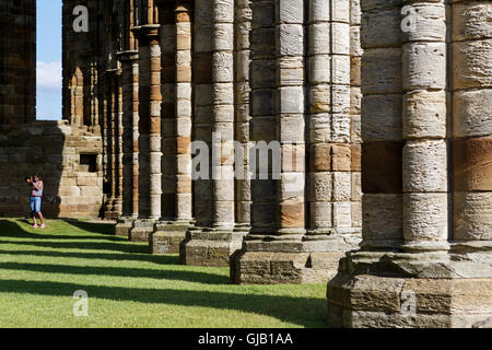 Young Asian girl taking a smartphone picture whilst visiting the ruins of Whitby Abbey. In Whitby, Stock Photo