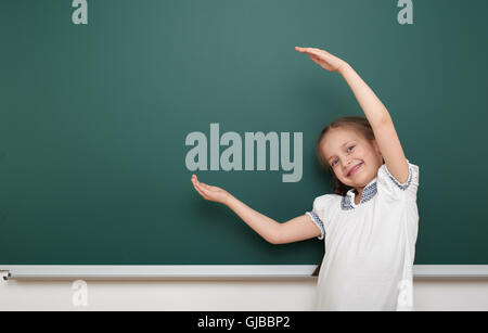 school student girl open arms at the clean blackboard, grimacing and emotions, dressed in a black suit, education concept, studi Stock Photo