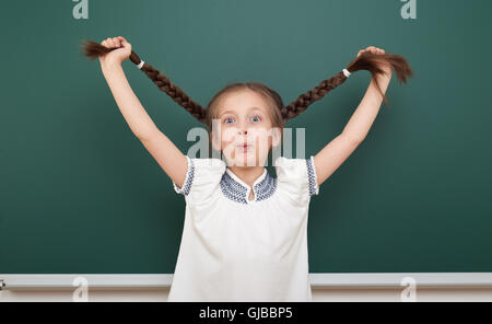 school student girl open arms at the clean blackboard, grimacing and emotions, dressed in a black suit, education concept, studi Stock Photo