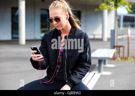 Blonde woman with sunglasses sits outdoor and uses phone Stock Photo