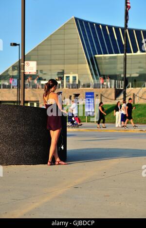 A young woman takes advantage of an outdoor electrical outlet to recharge her cell phone while also using the device. Chicago, Illinois, USA. Stock Photo