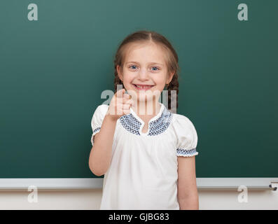 school student girl posing at the clean blackboard, grimacing and emotions, dressed in a black suit, education concept, studio p Stock Photo