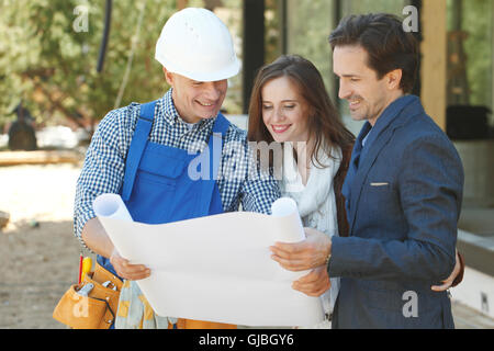 Worker shows house design plans to a young couple outdoors Stock Photo