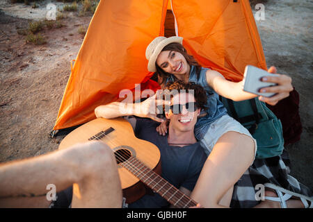 Happy young couple making selfie with smartphone and having fun camping by a lake Stock Photo