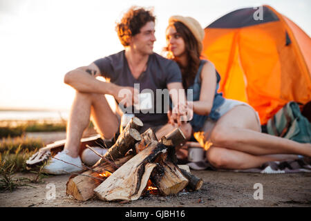 Young happy couple drinking tea at the bonfire and looking at each other while camping Stock Photo