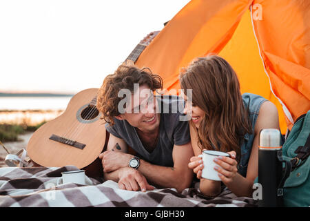 Happy young couple lying and drinking tea in touristic tent on the beach Stock Photo