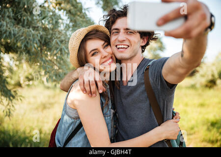 Young smiling happy couple with backpacks hiking in the forest and making selfie Stock Photo