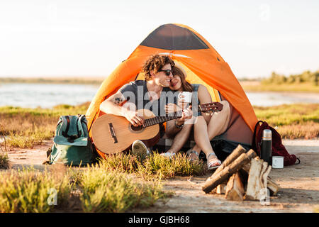 Portrait of a man playing guitar for his girlfriend camping at the beach Stock Photo