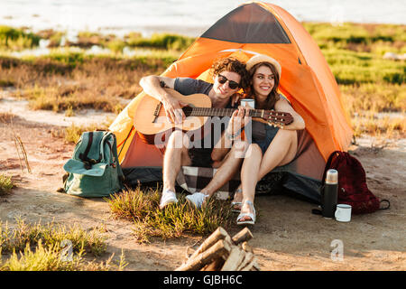 Portrait of a man playing guitar for his girlfriend sitting at the camping tent Stock Photo