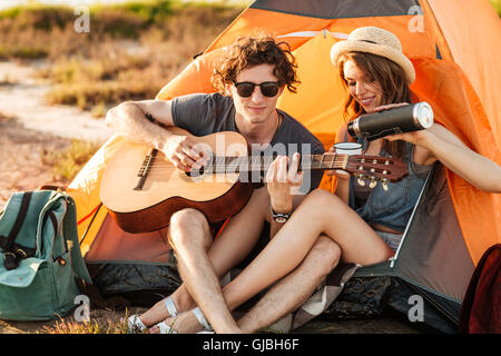 Portrait of a man playing guitar for his girlfriend camping at the beach Stock Photo