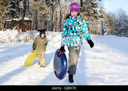 Girl and boy riding with hills on sleds on winter weather Stock Photo