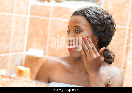 happy young woman applies cream on her face in the bathroom. Stock Photo