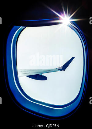 View from inside a plane looking out.  The wing,  a light-flare on the frame make an interesting, airborne composition in blue and white. Flying high. Stock Photo