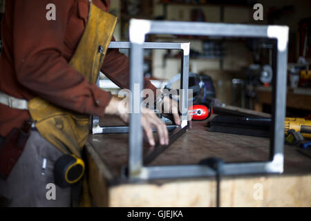 Custom furniture craftsman assembles stool support structure. Stock Photo