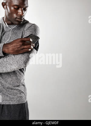 Shot of young black male model listening to music on cell phone. Man with mobile phone armband standing against grey background Stock Photo