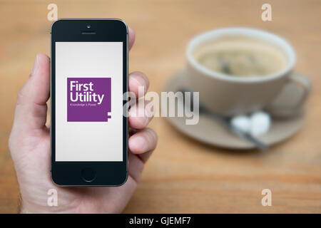 A man looks at his iPhone which displays the First Utility logo, while sat with a cup of coffee (Editorial use only). Stock Photo
