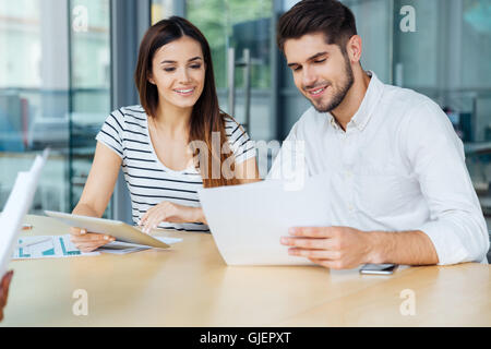 Smiling young couple with tablet sitting at the table and working in office Stock Photo