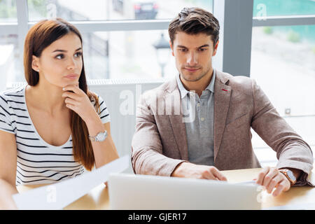 Concentrated pensive woman and man working and discussing project and using laptop in the office Stock Photo