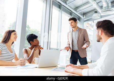 Smiling handsome young businessman standing and making presentation to his colleagues in conference room Stock Photo