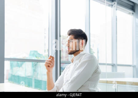 Serious pensive young businessman sitting and thinking in office Stock Photo