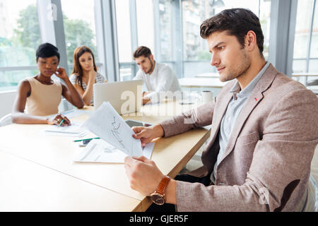 Concentrated young businessman sitting and creating presentation with his business team in office Stock Photo