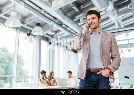 Happy young businessman standing and talking on cell phone in office Stock Photo