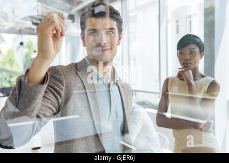 Concentrated young businessman working with african businesswoman and writing on transparent board in office Stock Photo