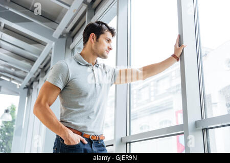 Thoughtful handsome young man standing and looking at the window Stock Photo