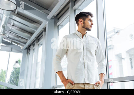 Serious pensive young man standing and thinking near the window Stock Photo