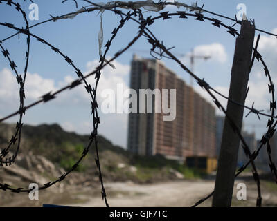 Abandoned construction site of an apartment building. The building is located behind a fence topped with barbed wire. Stock Photo